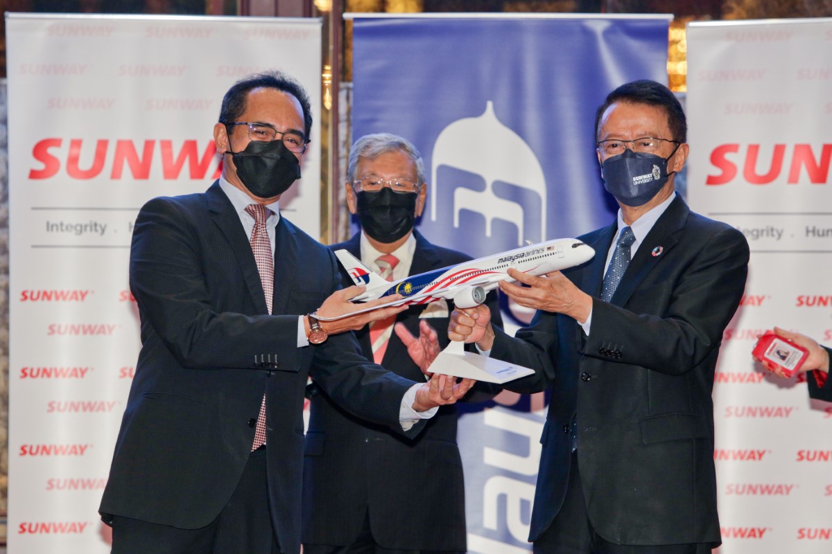 A medium full landscape shot of Sunway Group founder and chairman Tan Sri Dr. Jeffrey Cheah (right) receiving an A350-900 model aircraft as a memento from Malaysia Aviation Group chairman Tan Sri Wan Zulkiflee bin Wan Ariffin (left), while Sunway Group deputy chairman Tan Sri Datuk Seri Razman M. Hashim (centre) looks on.