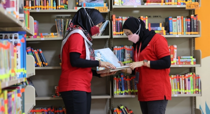 A medium full landscape shot of two Sunway volunteers in classic red polo, leafing through pages of donated books in a newly-furnished library at Sekolah Menengah Kebangsaan Yaacob Latif in Cheras, Kuala Lumpur.