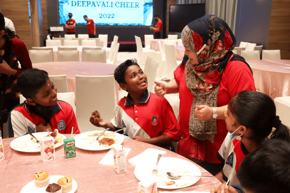 A candid shot of a Sunway staff alongside children talking about the food in the hall. Containing food such as muffin and packet drinks.