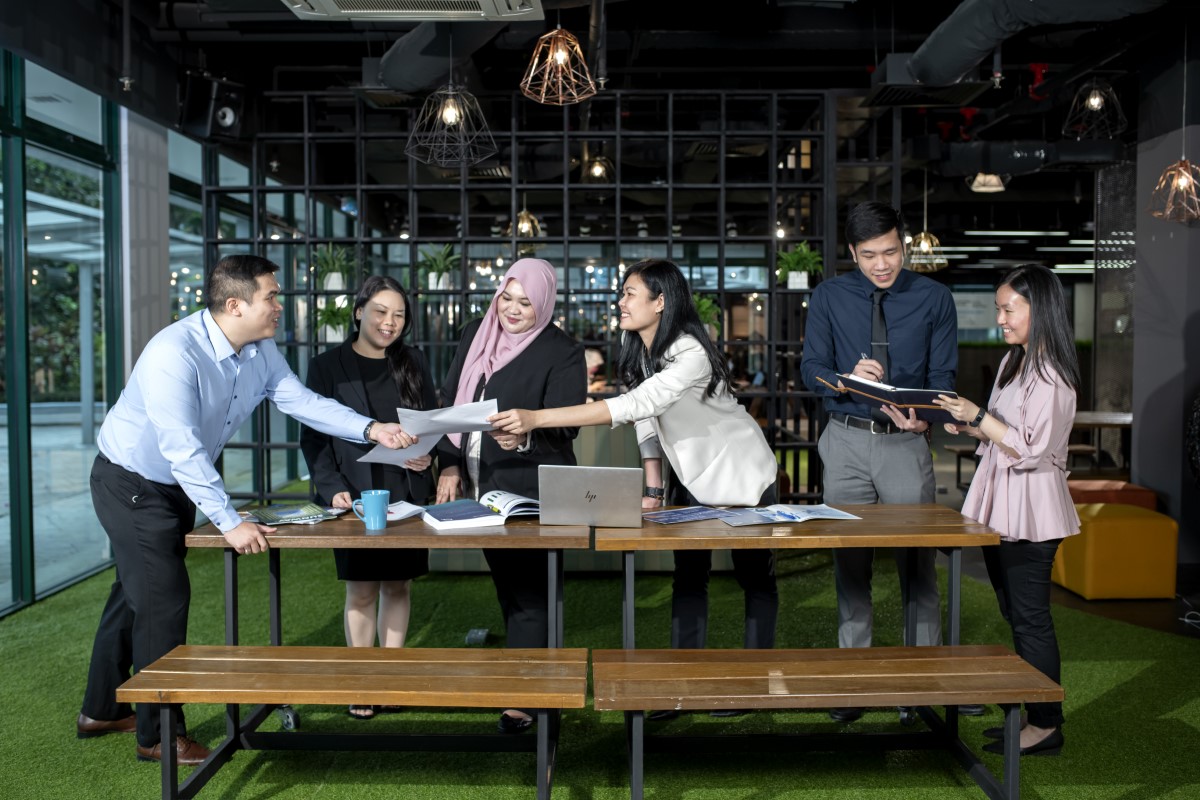 Sunway staff discussing business plans across a table, with laptops books and papers in place