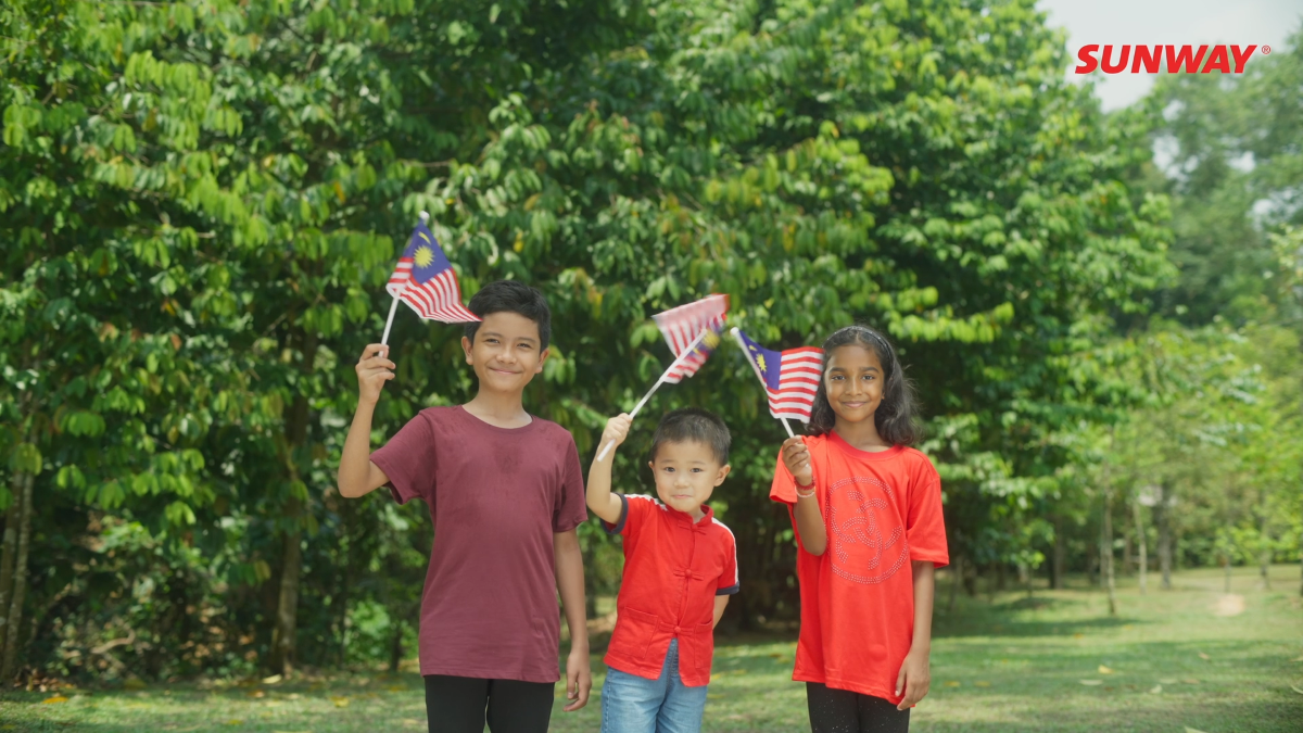 Three children waving the Malaysian flag, with greeneries and trees in the background