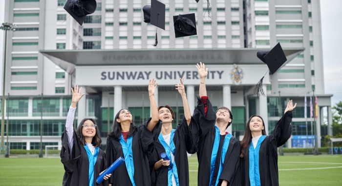 Sunway students in graduation robes throwing their graduation cap, with Sunway University building in the background