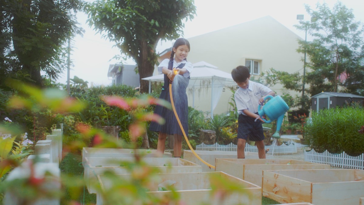 A Chinese girl, Xiao Wei (left) and a Malay boy, Ahmad (right) are filled with joy as they work together to water their crops amidst a field of green