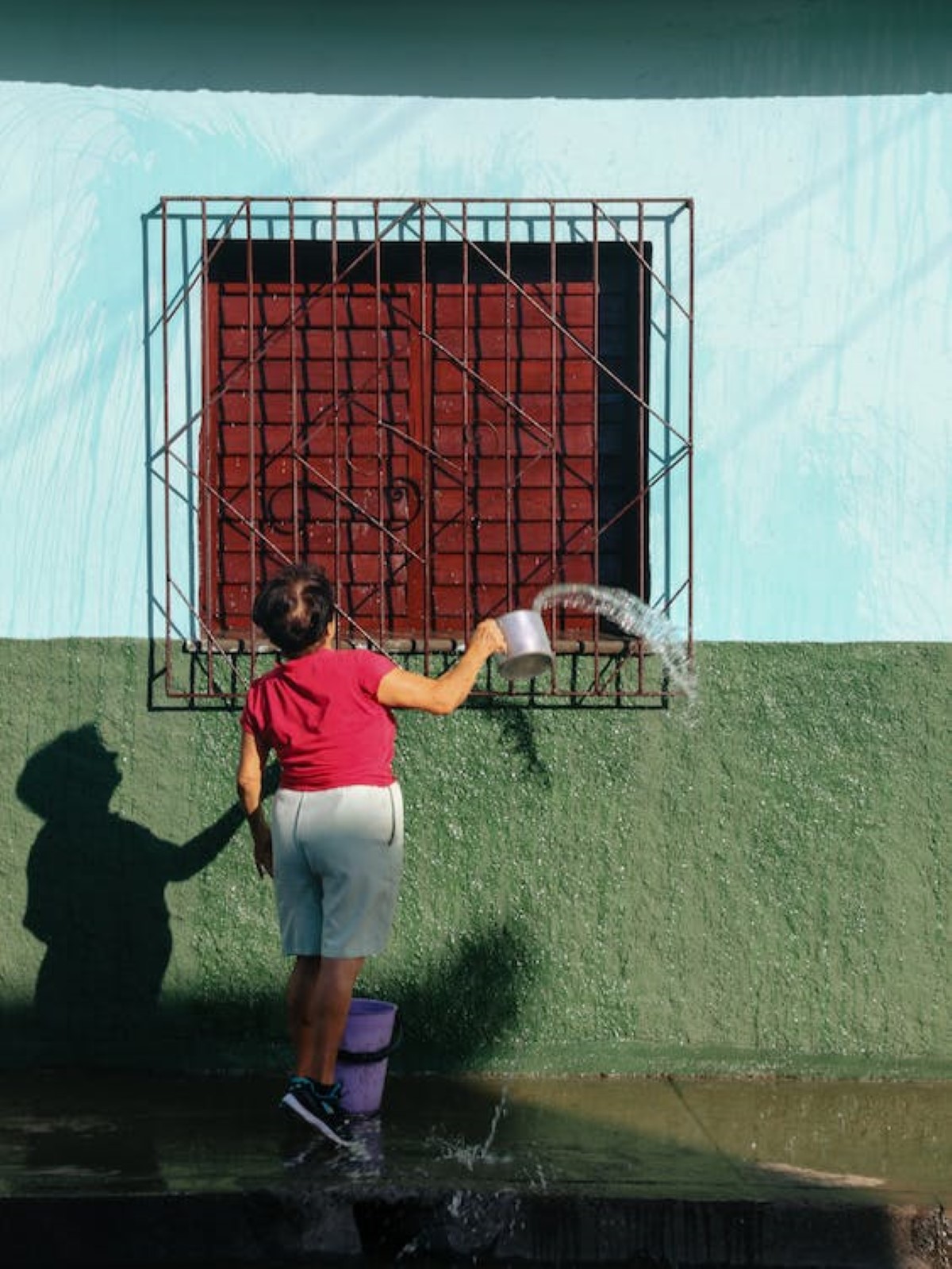 A full portrait shot of a person throwing water onto a window fixture during daytime