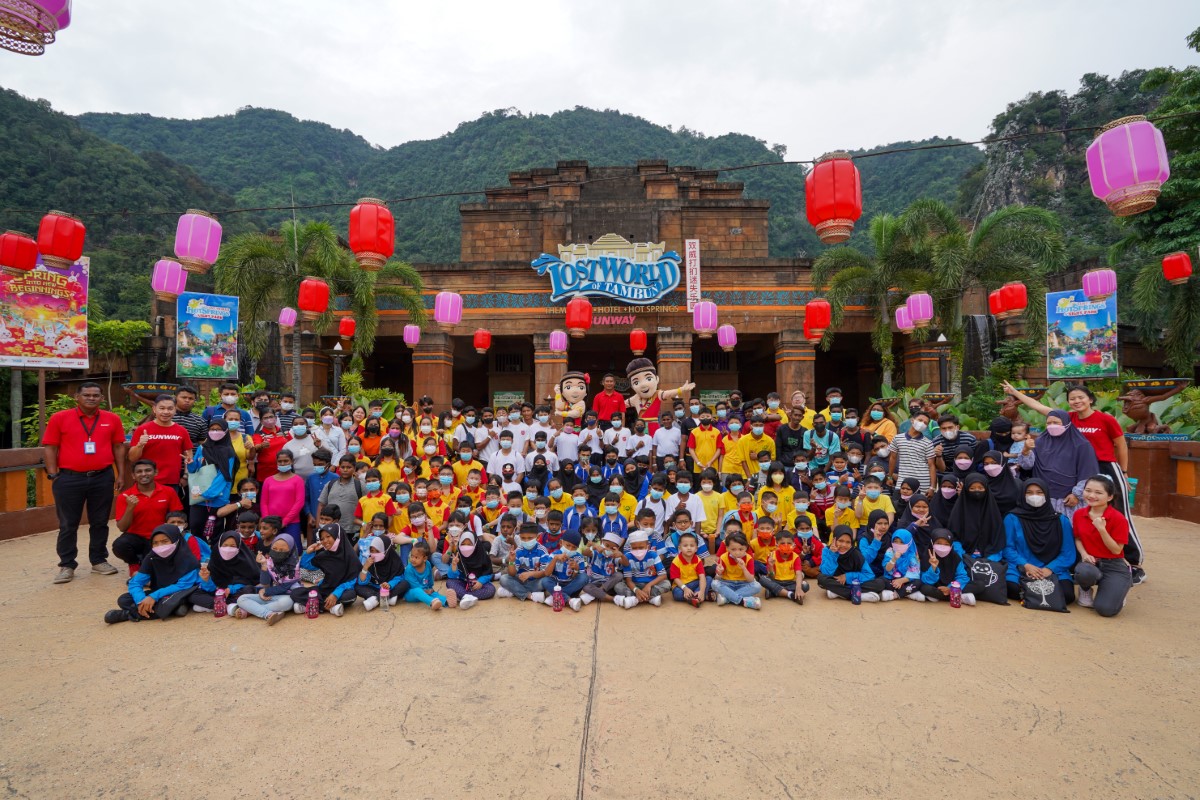 More than 250 underprivileged children from eight orphanages, alongside Sunway staff clad in red, present for #SunwayforGood CNY Cheer 2023 initiative in Lost World Tambun facade decorated with red lanterns.