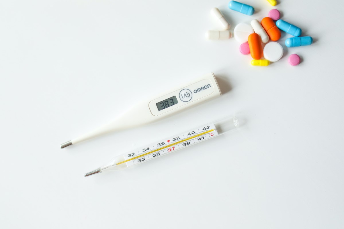A full landscape shot of thermometers and colourful pills atop a white surface