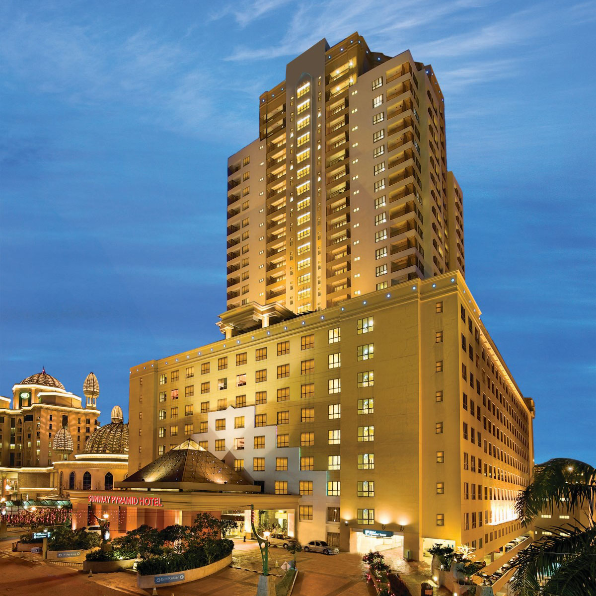 Façade of Suway Pyramid Hotel amid the dusky blue sky, with lights adorning the building.