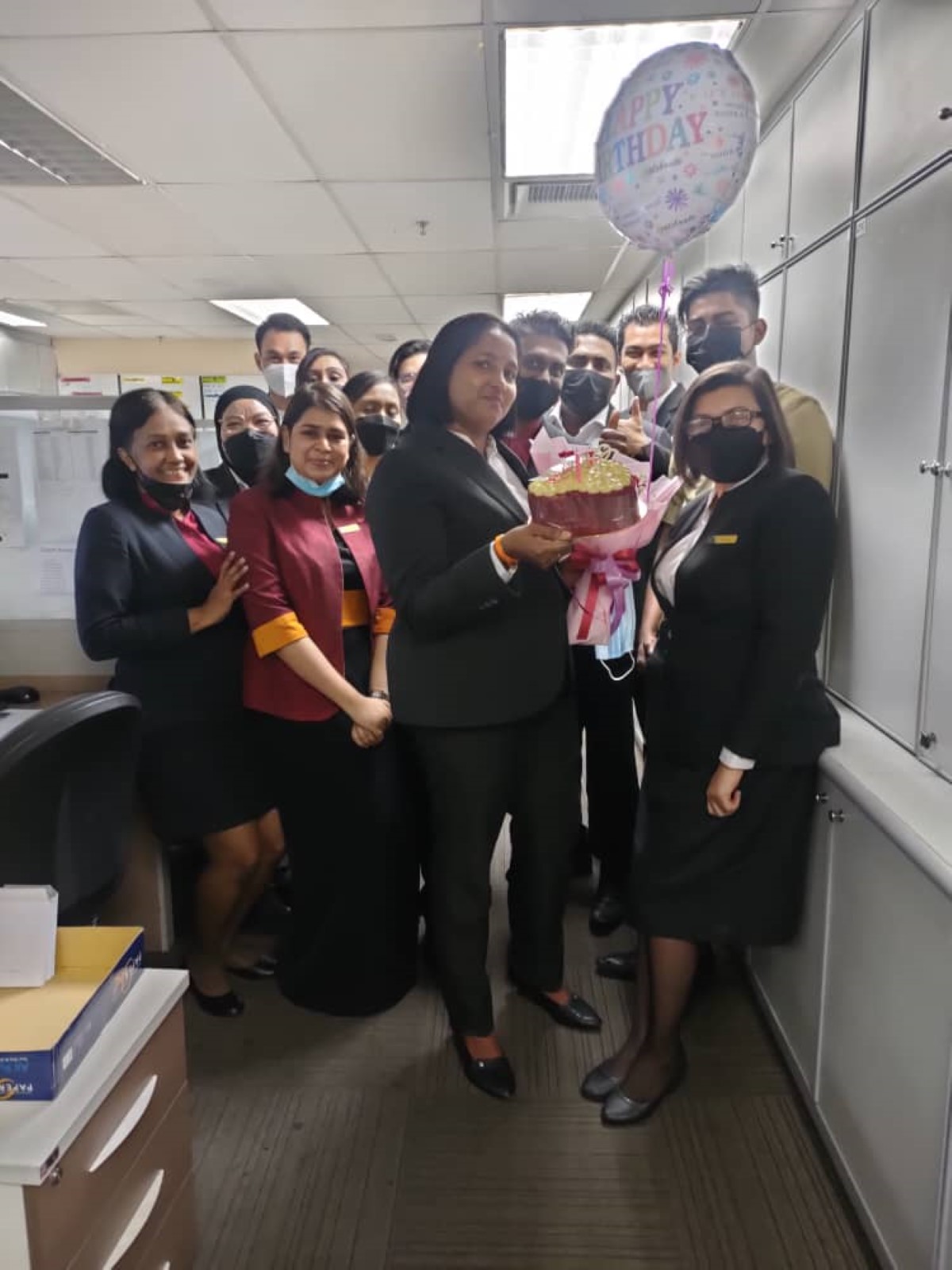 Shanta alongside her colleagues celebrating her birthday, holding a birthday cake and some balloons.