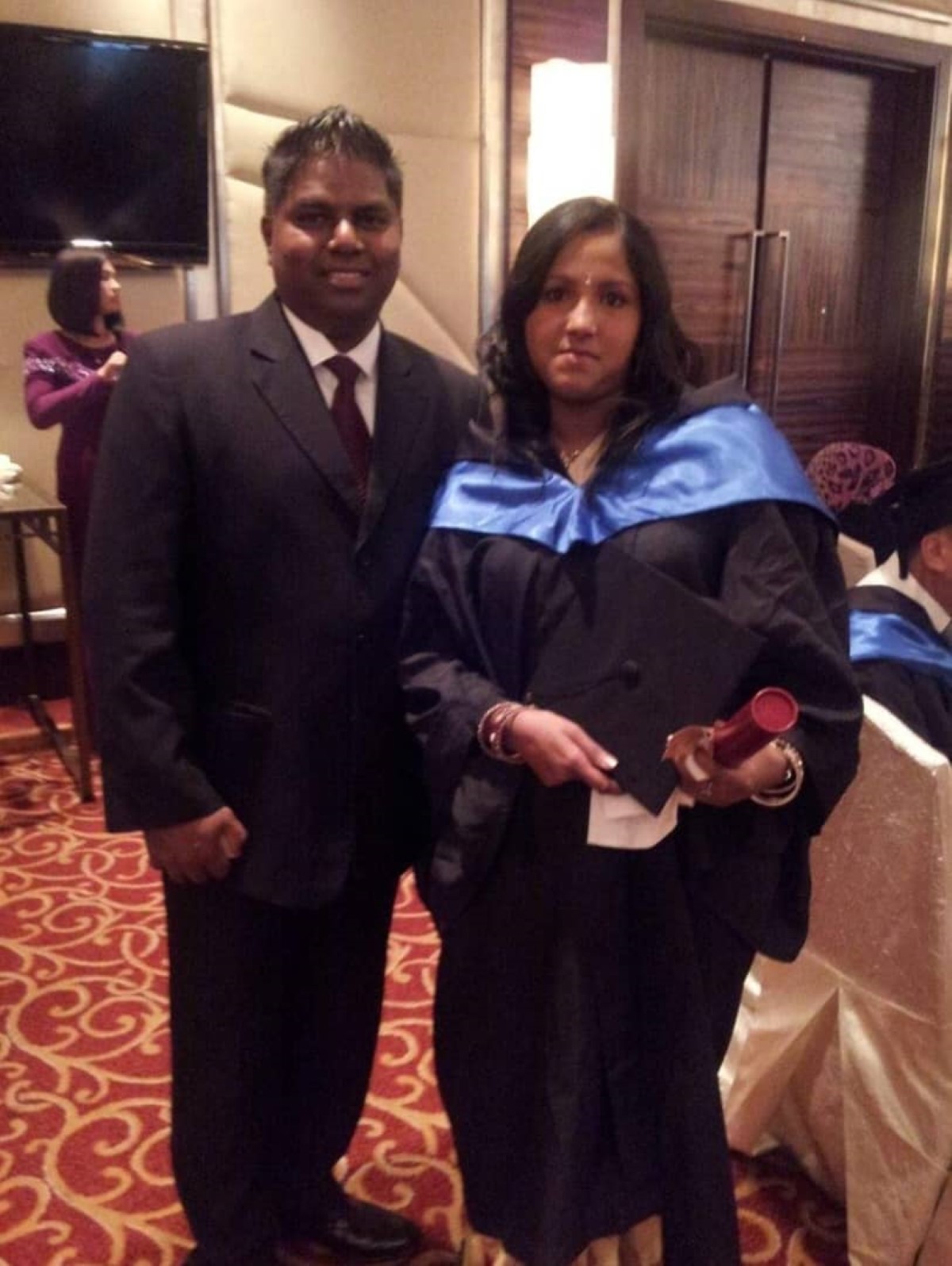 Shanta alongside a man at her graduation ceremony, dressed in her graduation robe.