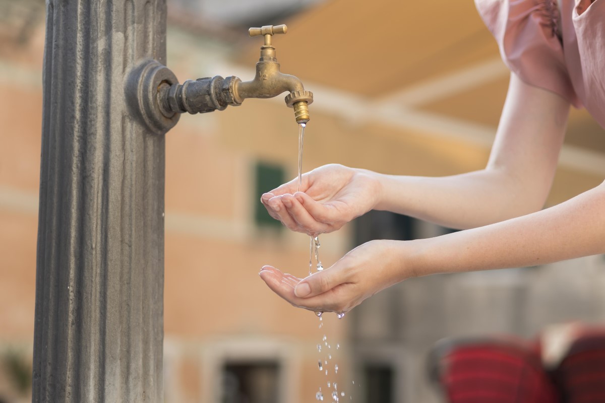 A woman getting water from a tap, although the water is not flowing as freely from the tap.