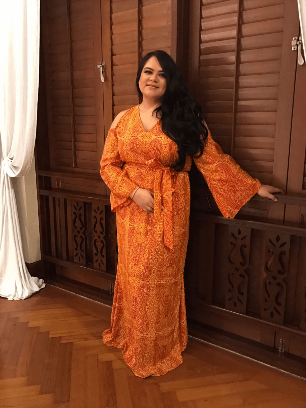 Melissa Hashim, senior manager of creative marketing at Sunway Malls in her orange dress, posing in front of wooden windows and white curtains