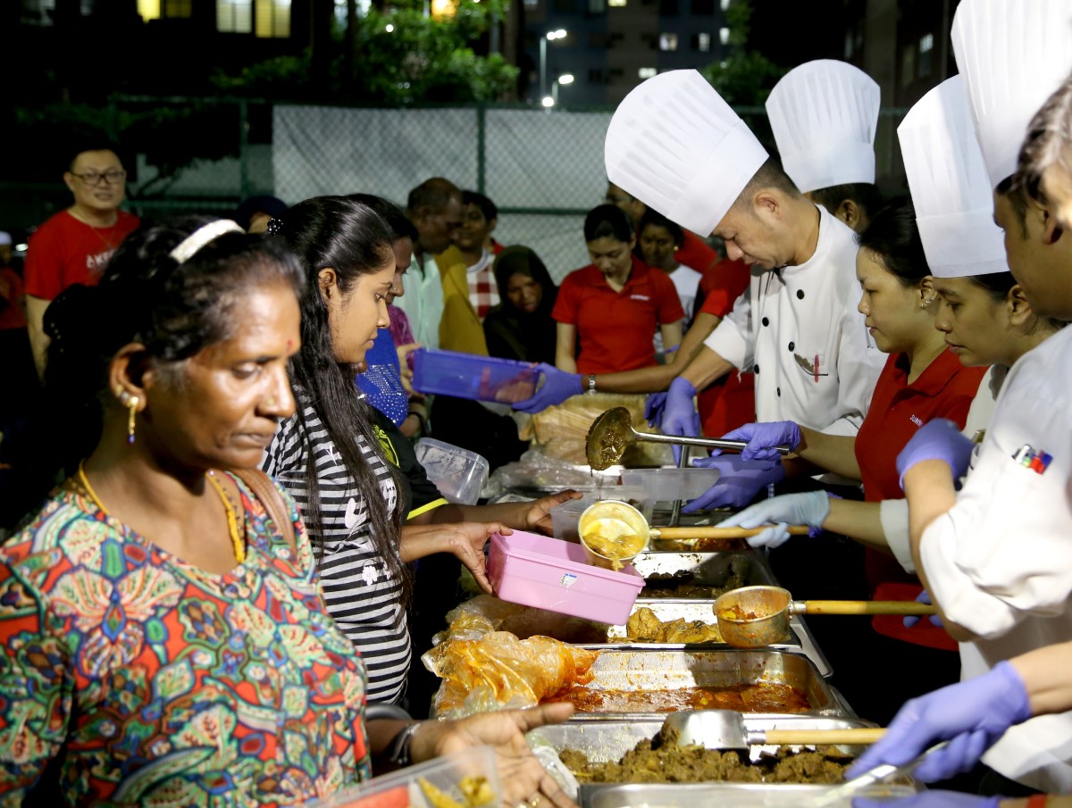 A medium landscape shot of Sunway volunteers and Sunway Resort Hotel chefs transferring surplus food in chafing dishes to the underprivileged and needy in the evening.