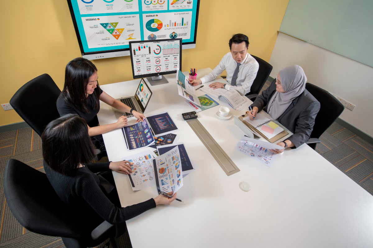 Sunway staff of three females and one male having an online meeting regarding FinTech and analysing data, with graphs and papers at their desk