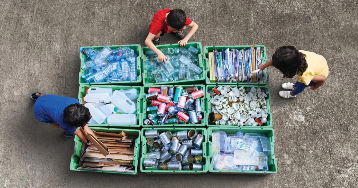 A stock image of three individuals sorting waste materials according to respective categories prior to recycling them.