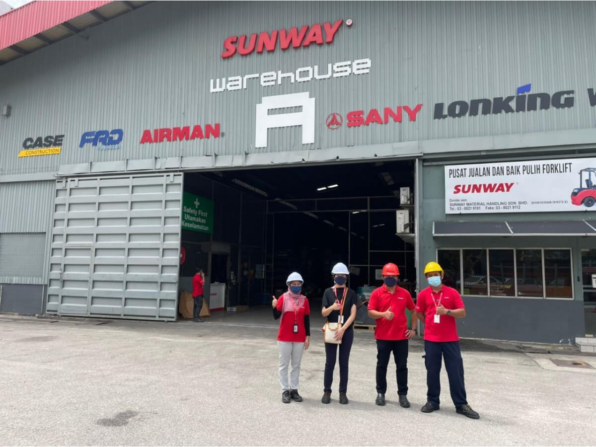 Sunway staff wearing hard hats at a Sunway warehouse, posing with thumbs up for the camera.
