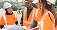 Four Sunway Construction team members of various races, clad in Sunway Construction orange reflector vest and Sunway hard hats at a construction site 