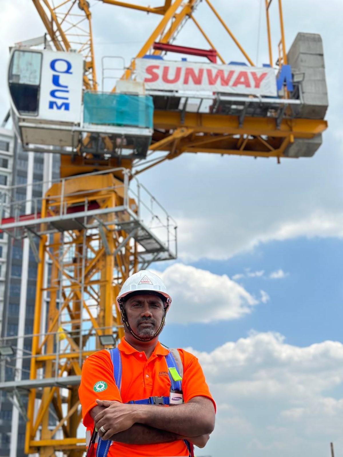 Sunway Construction’s Environment, Safety and Health (ESH) general manager Mr. Kalaiselvan wearing a white hard hat at a Sunway Construction site, with a crane and Sunway logo in the background