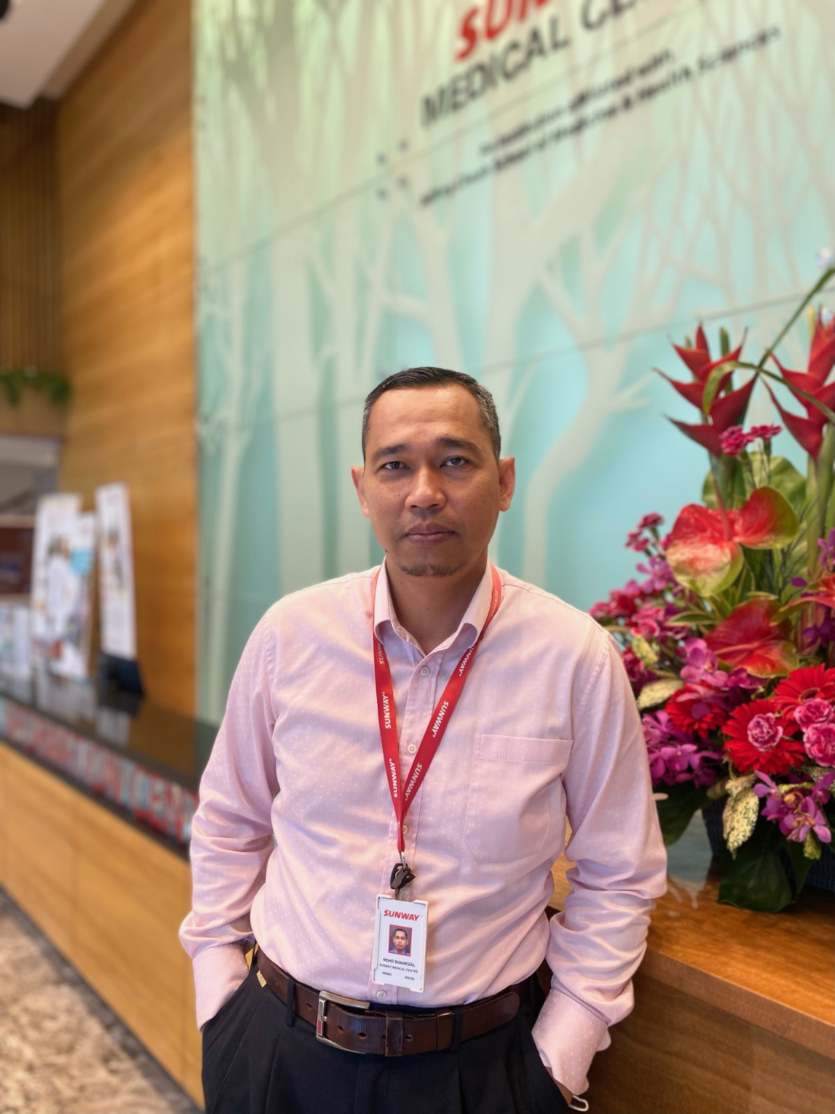 Captain Shahrizal, Sunway Medical Centre ESH manager posing in front of the Sunway Medical Centre lobby façade, with flowers in the background