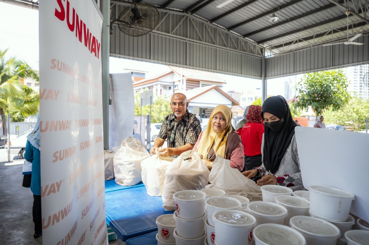 Bubur lambuk alongside volunteers to distribute to the underserved communities, with the Sunway banner in the foreground.