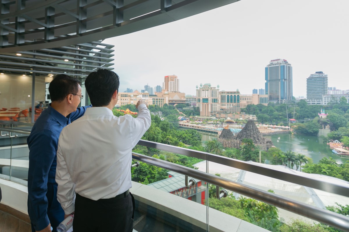 Tan Sri Dr. Jeffrey Cheah, clad in blue, showcasing Sunway City Kuala Lumpur to a stakeholder. With SCKL brimming with green trees and Sunway Resort Hotel, Sunway Pinnacle & Menara Sunway in the background.
