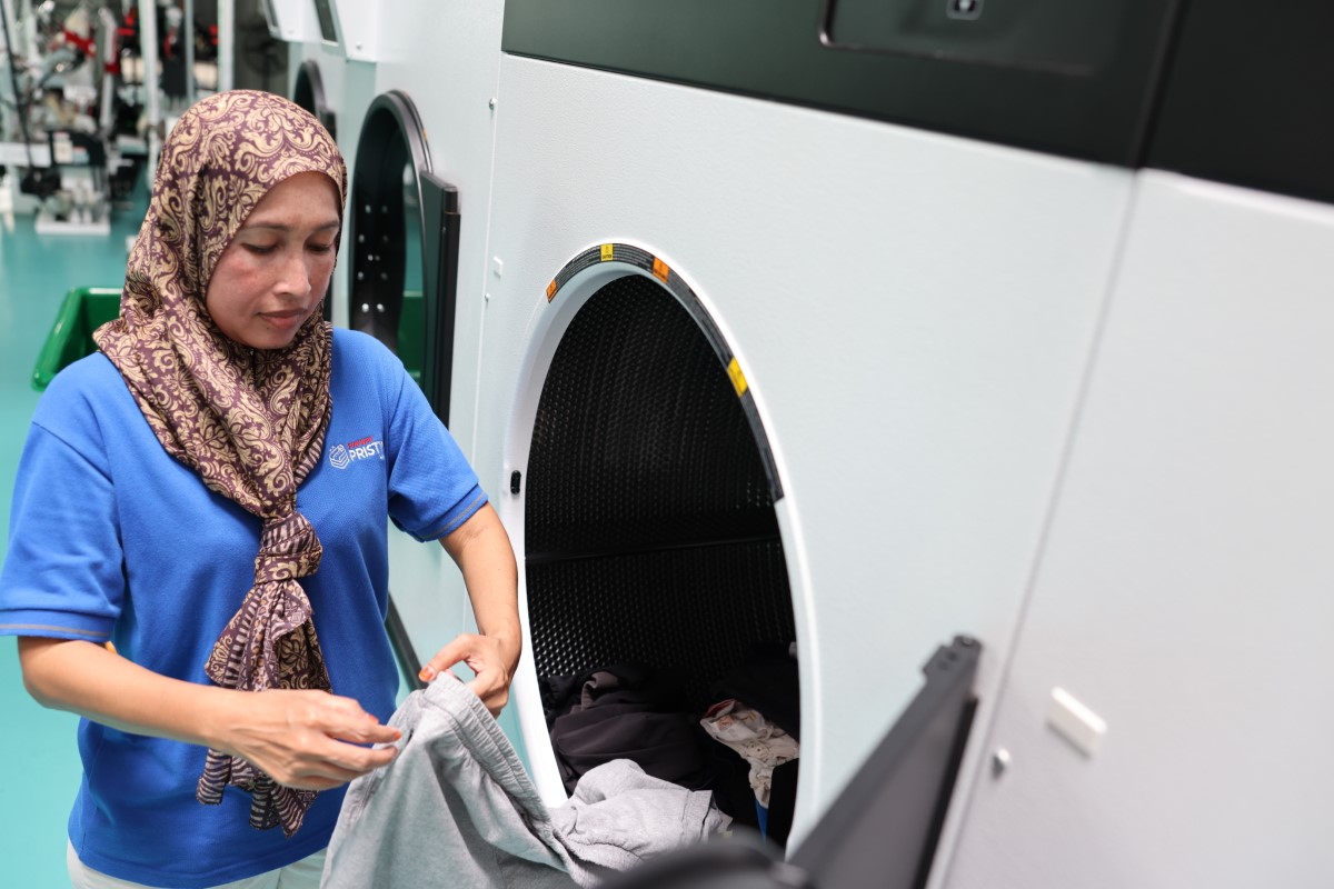 A medium landscape shot of a Sunway Pristine Laundry staff feeding laundry into an industrial front load washing machine.