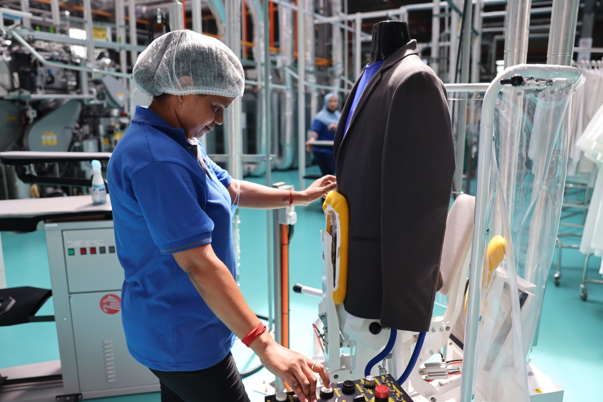 A medium full landscape shot of a Sunway Pristine Laundry staff carefully steaming and pressing a blazer suit using a Sankosha industrial steamer.