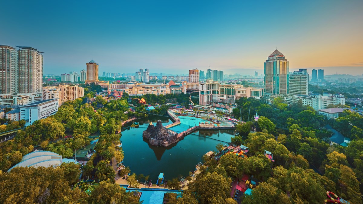 A drone shot of Sunway Lagoon lake at Sunway City Kuala Lumpur, with the city in full view and green trees around.