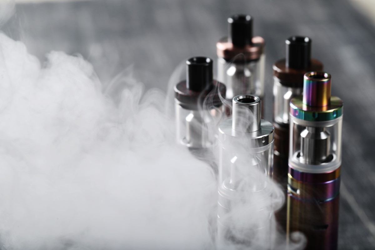 A close-up shot of five vape machines with white smoke in the foreground.