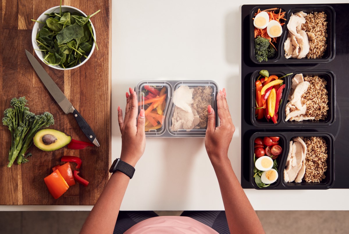 A top down shot of meal prepping, with vegetables and a tupperware in the middle