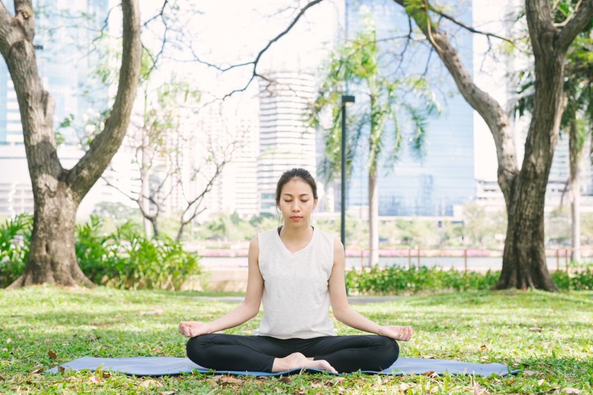 a far shot of a female doing yoga, amidst trees and a lush background