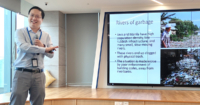 A midshot of Dr. Chen giving a presentation at Sunway Pinnacle, with a TV monitor in the background and parquet tiles