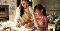 A mother and her child making food, with a rolling pin in hand and bowls alongside them