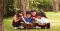 A group of children reading a book in a green field