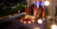 A far shot of an Indian family standing amidst the kolam, in a nicely lit house