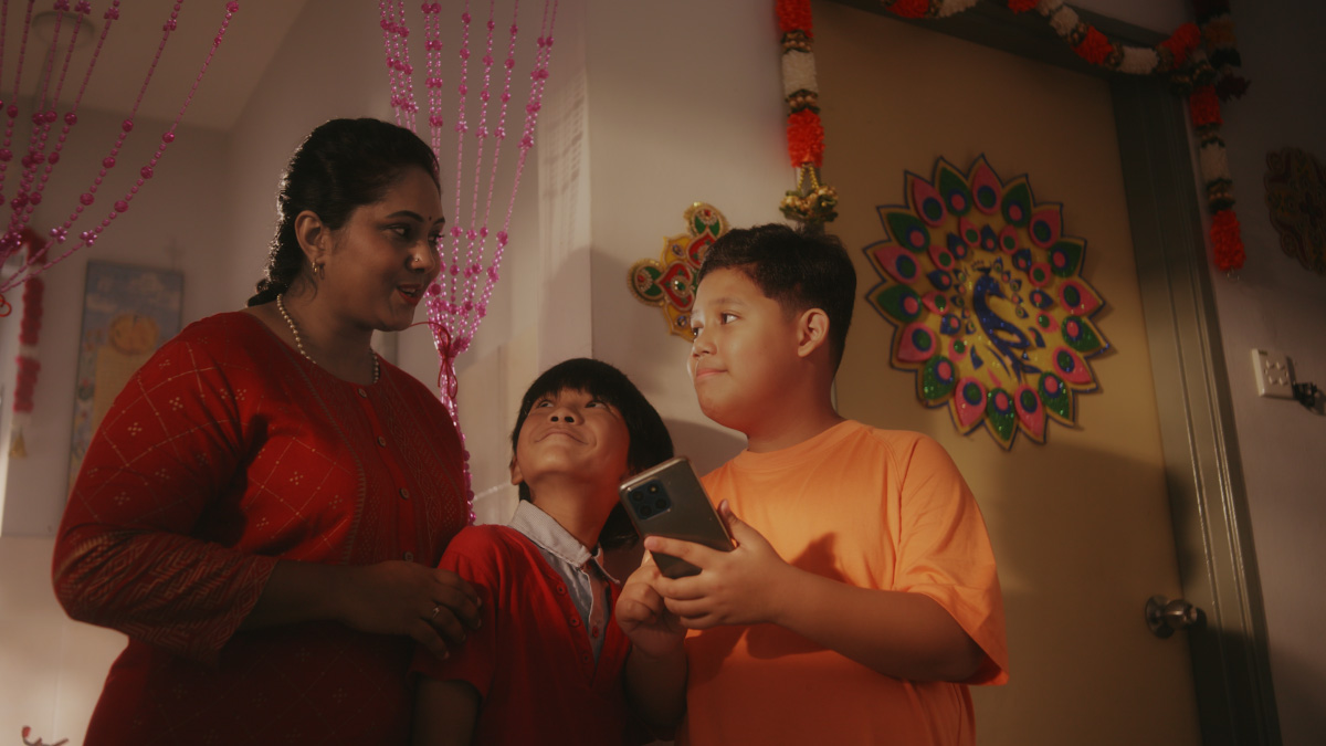 A mid shot of Priya's friends showing the mother how to use the Sunway Super App, amidst a warm lighting at Priya's house