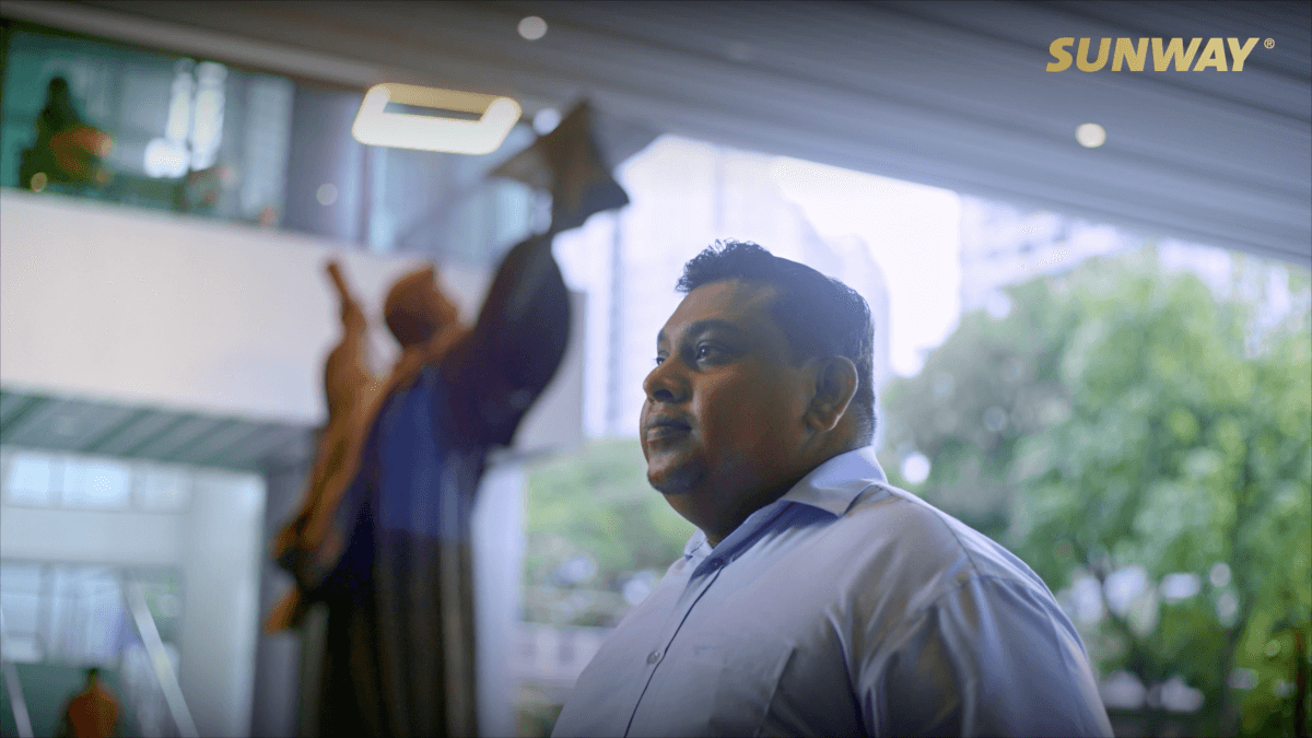 Shows a midshot of Jagadesan, an alumnus of Sunway University, standing at the foyer of Sunway University, with the Destiny statue in the background