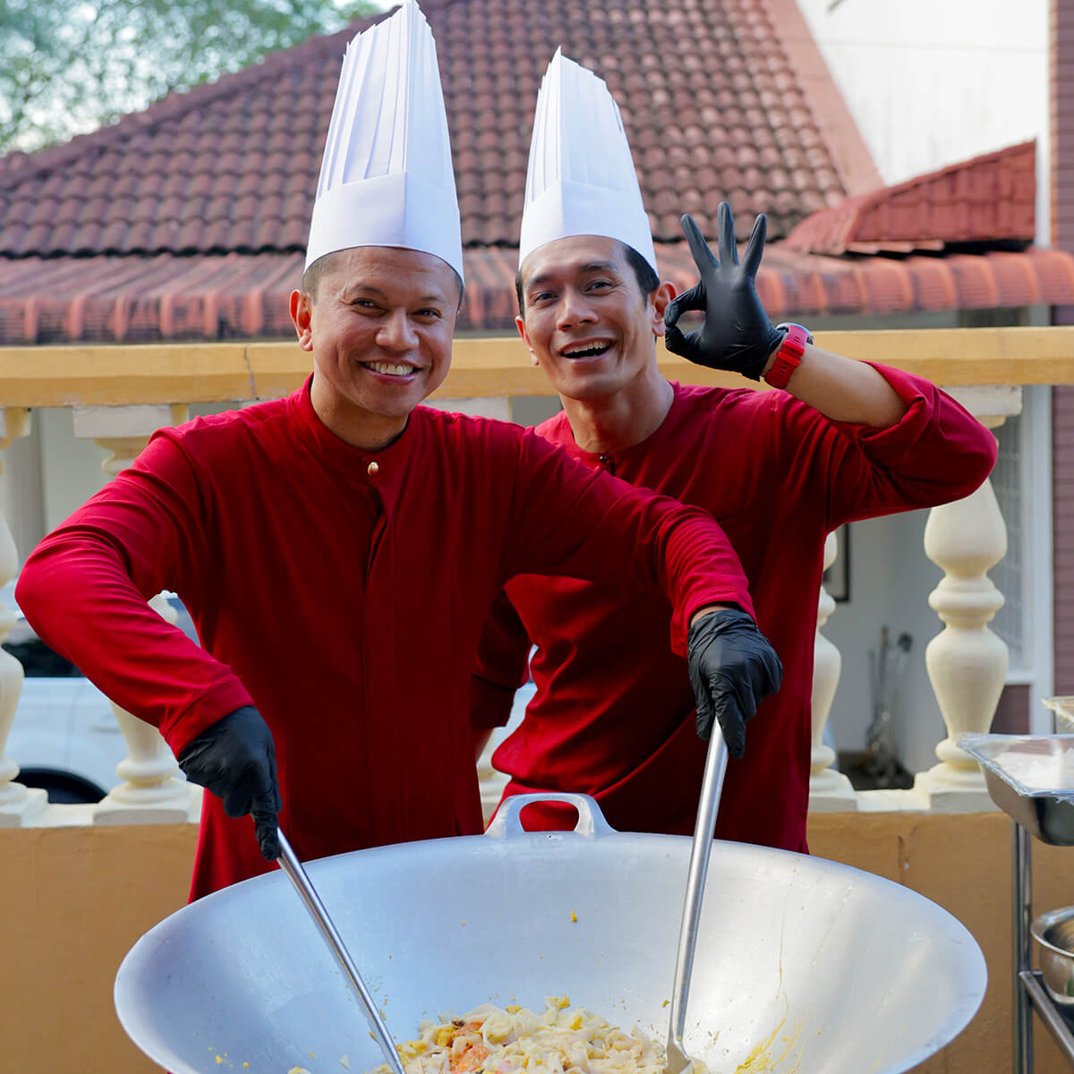 A mid-shot of Fahrin Ahmad and Shah Shamshiri cooking and smiling for the camera.