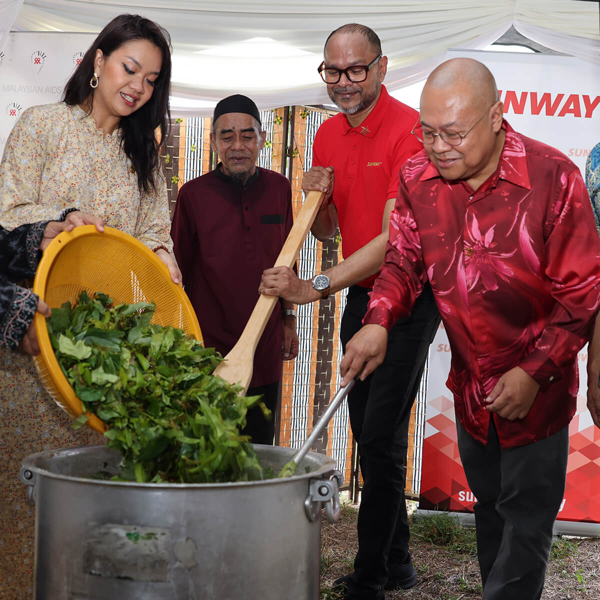 A full body shot of Mimi Fly alongside Sunway and Malaysian AIDS Foundation senior leaders stirring bubur lambuk