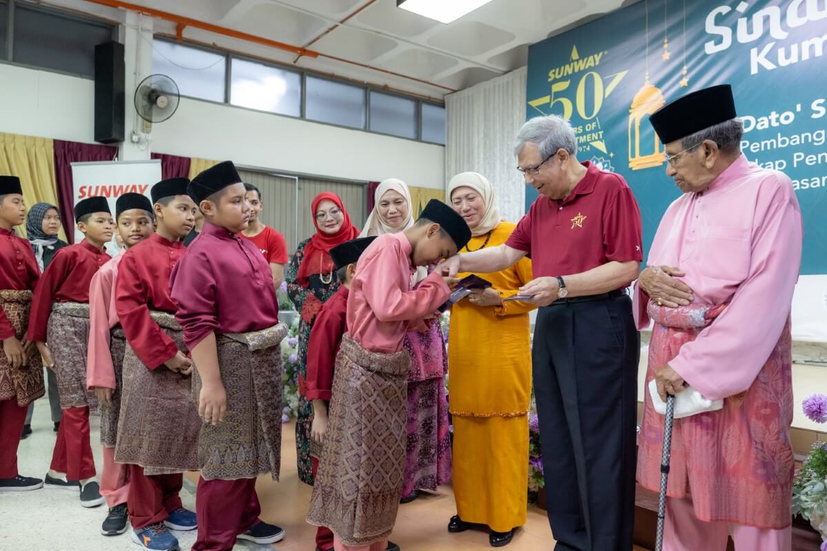 A mid-shot of Sunway Group deputy chairman Tan Sri Razman gifting duit Raya to the children alongside Minister of Women, Family and Community Development YB Dato' Sri Hajah Nancy Binti Shukri