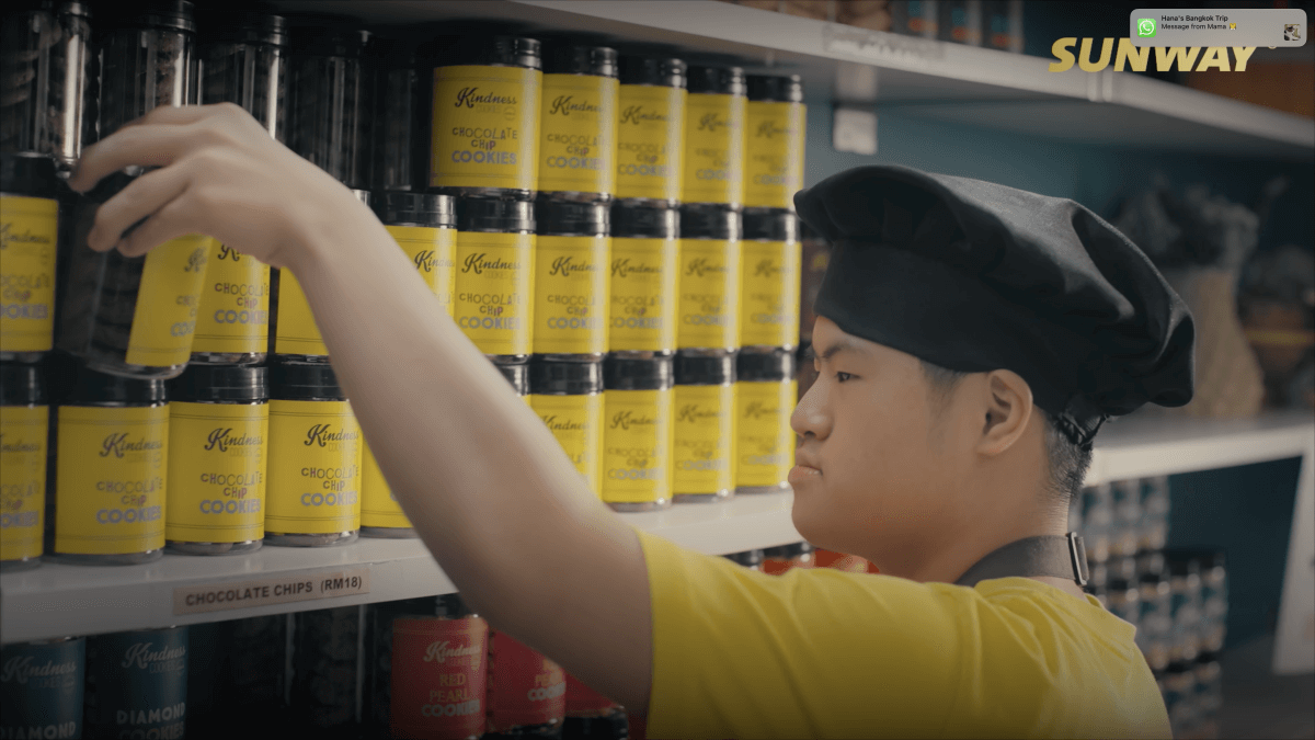 A mid-shot of Sing Hon arranging cookies at the shelf.