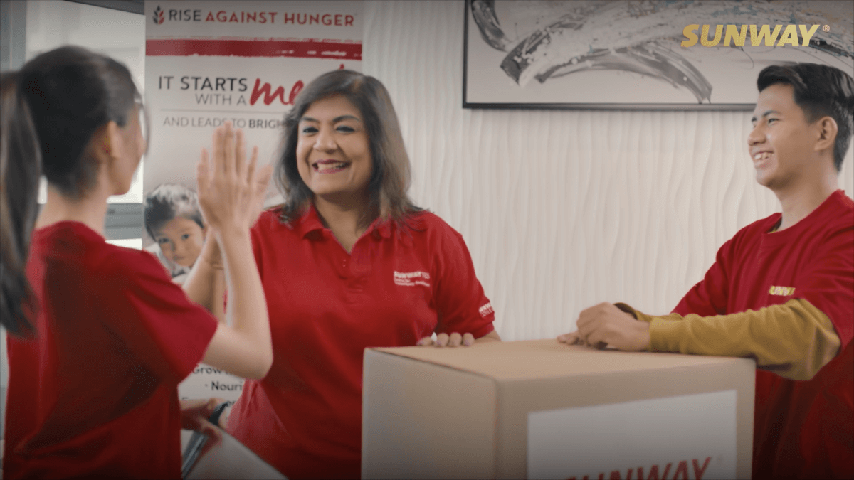 A mid-shot of Kiran and two other Sunway volunteers packing boxes and giving high-fives.